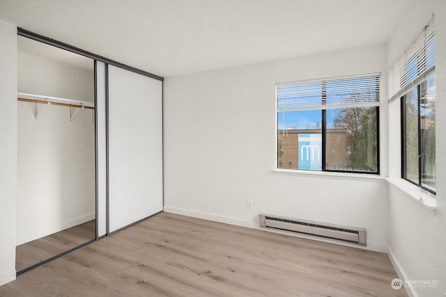 unfurnished bedroom with a baseboard heating unit, light hardwood / wood-style floors, and a closet