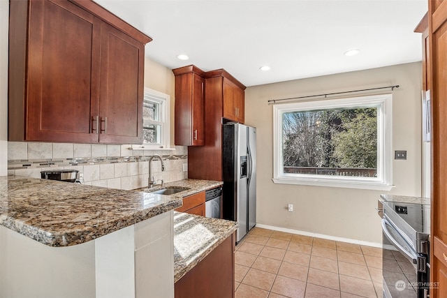 kitchen featuring sink, appliances with stainless steel finishes, tasteful backsplash, light stone countertops, and kitchen peninsula