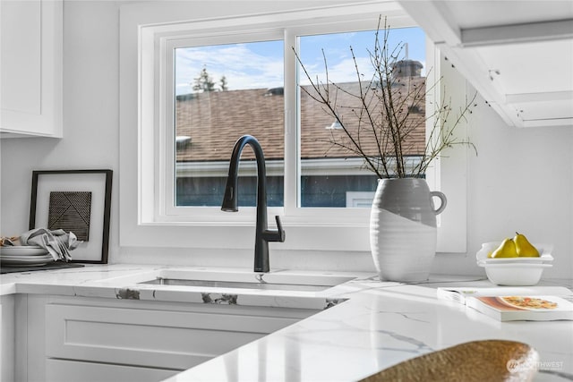 interior details with sink, light stone countertops, and white cabinets