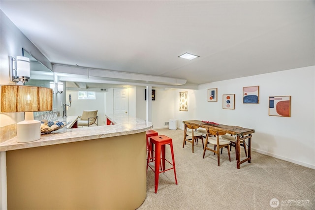 kitchen with a kitchen bar, light countertops, light carpet, a peninsula, and baseboards