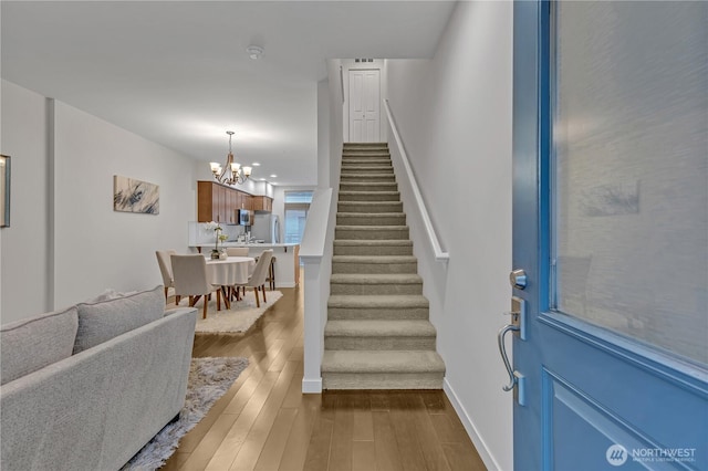 entrance foyer featuring an inviting chandelier, baseboards, stairway, and dark wood-style flooring