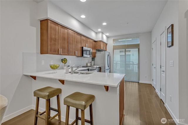 kitchen with backsplash, appliances with stainless steel finishes, brown cabinetry, a peninsula, and a kitchen breakfast bar