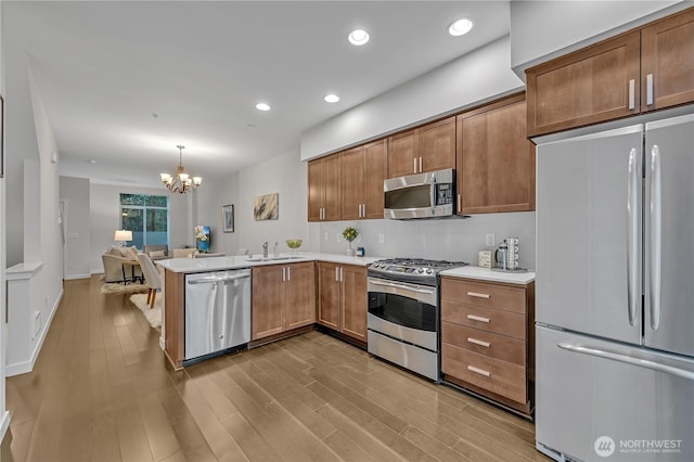 kitchen featuring stainless steel appliances, light countertops, a peninsula, and wood finished floors