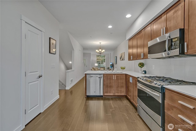 kitchen featuring dark wood-style floors, brown cabinets, stainless steel appliances, tasteful backsplash, and a peninsula