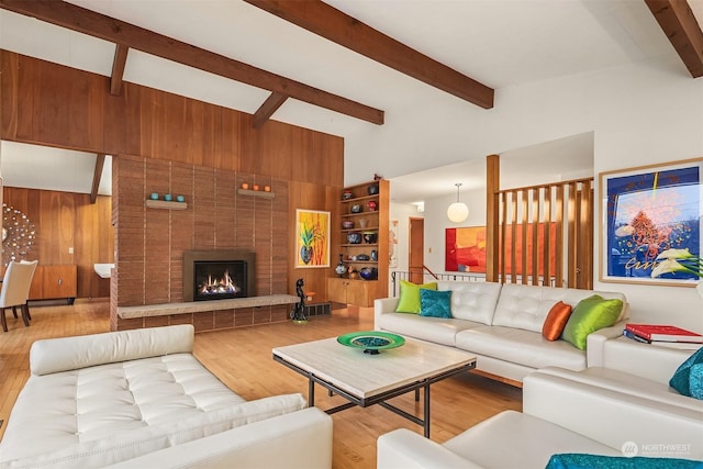 living room featuring hardwood / wood-style flooring, a brick fireplace, lofted ceiling with beams, and wood walls