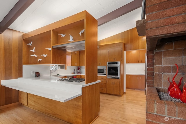 kitchen featuring appliances with stainless steel finishes, wood walls, sink, kitchen peninsula, and light wood-type flooring