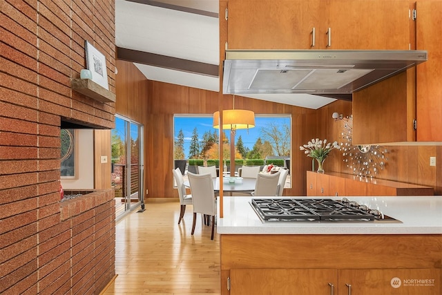 kitchen featuring stainless steel gas stovetop, wood walls, light wood-type flooring, and lofted ceiling with beams