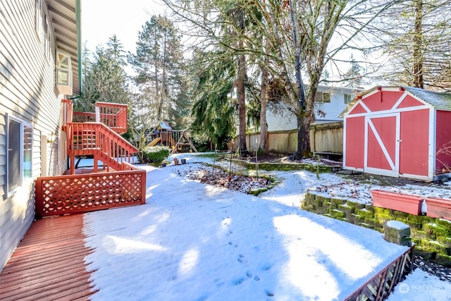 yard covered in snow featuring a playground, a wooden deck, and a shed