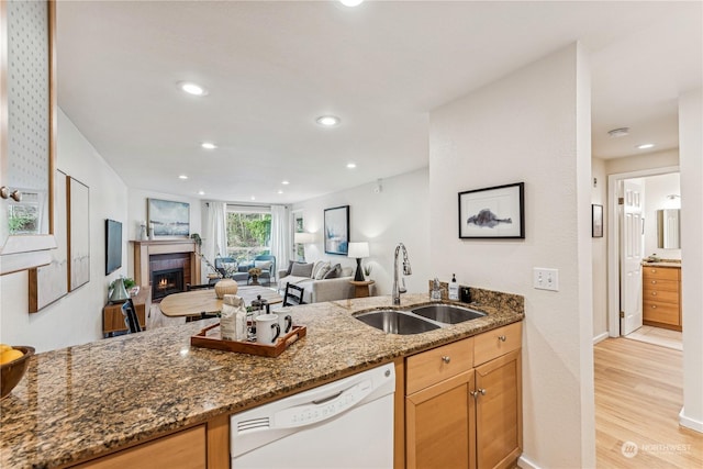 kitchen with sink, light hardwood / wood-style flooring, dishwasher, dark stone counters, and a fireplace