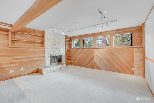 unfurnished living room featuring a wealth of natural light, wooden walls, and carpet flooring