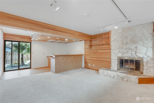 unfurnished living room with light carpet, a fireplace, bar, and wood walls