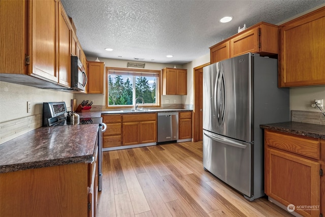 kitchen featuring stainless steel appliances, sink, light hardwood / wood-style flooring, and a textured ceiling