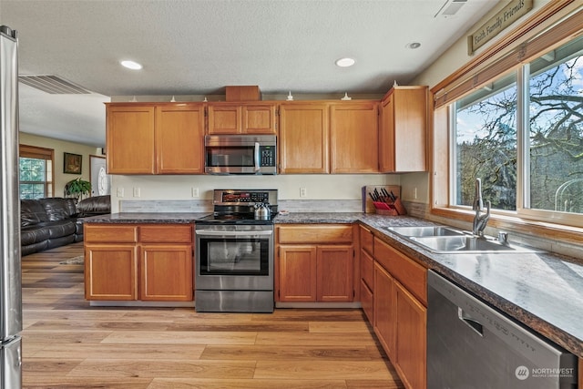 kitchen with stainless steel appliances, sink, a textured ceiling, and light wood-type flooring