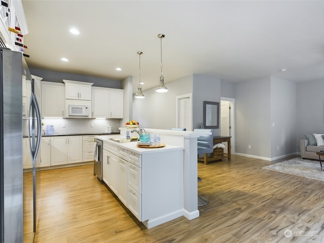 kitchen with sink, white cabinetry, decorative light fixtures, light wood-type flooring, and stainless steel appliances