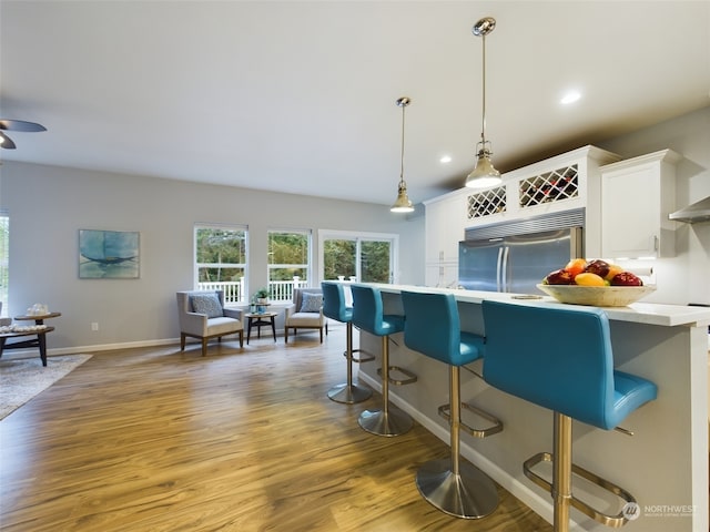 kitchen featuring built in refrigerator, white cabinetry, a breakfast bar, and decorative light fixtures