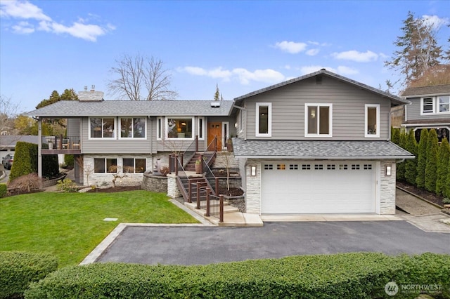 tri-level home featuring aphalt driveway, roof with shingles, a chimney, an attached garage, and a front yard