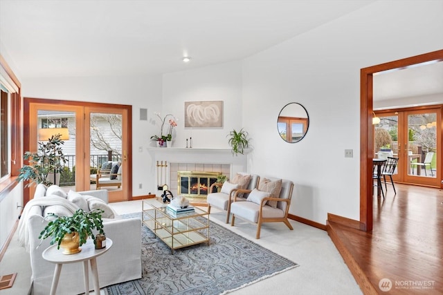 living room with lofted ceiling, french doors, a tile fireplace, and baseboards