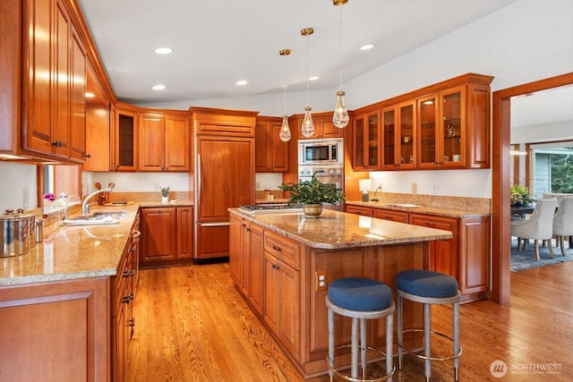 kitchen featuring brown cabinetry, a kitchen island, built in appliances, light wood-style floors, and a sink