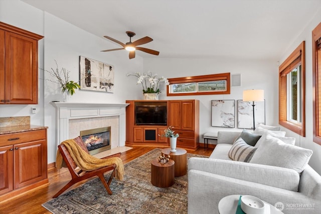 living area featuring lofted ceiling, a tiled fireplace, a ceiling fan, and wood finished floors