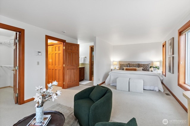 bedroom featuring a walk in closet, a closet, light colored carpet, visible vents, and baseboards