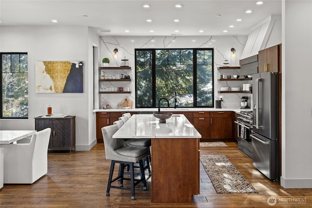 kitchen featuring high quality appliances, a kitchen island, dark wood-type flooring, and a breakfast bar area