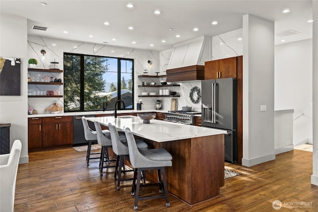 kitchen with high end appliances, dark hardwood / wood-style floors, a kitchen breakfast bar, and custom range hood