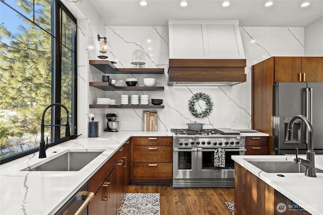 kitchen featuring sink, premium range hood, appliances with stainless steel finishes, a wealth of natural light, and light stone countertops