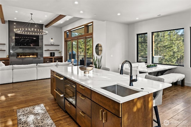 kitchen with beamed ceiling, sink, a kitchen bar, a kitchen island with sink, and dark wood-type flooring