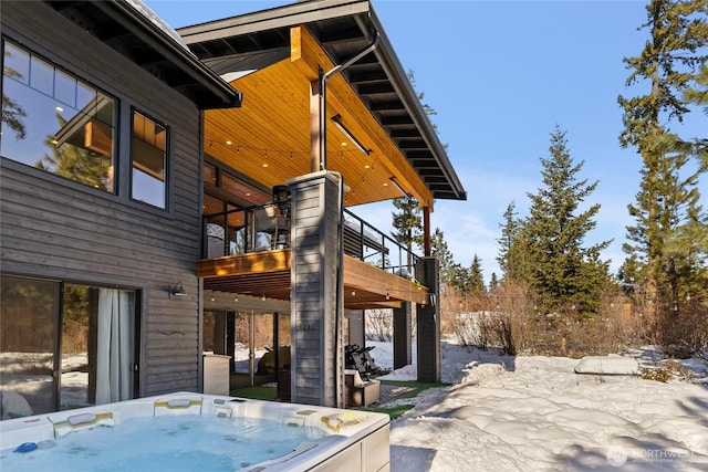 snow covered patio featuring a balcony and a hot tub