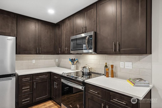 kitchen featuring stainless steel appliances, dark brown cabinets, backsplash, and light hardwood / wood-style flooring