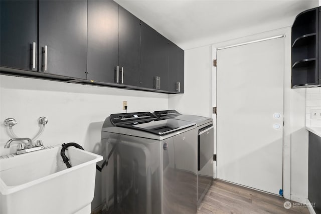 clothes washing area featuring cabinets, washing machine and clothes dryer, sink, and light wood-type flooring