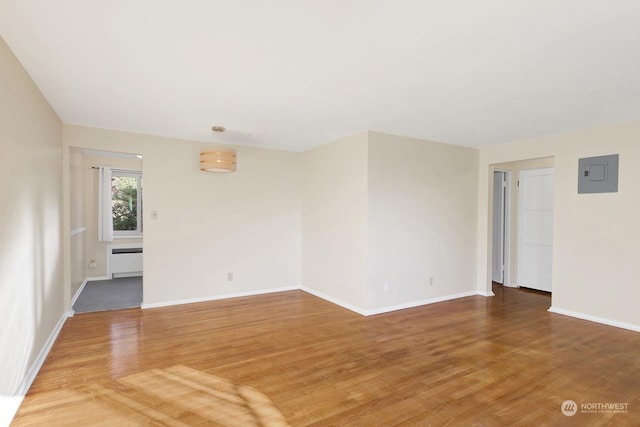 spare room with radiator heating unit, electric panel, and wood-type flooring