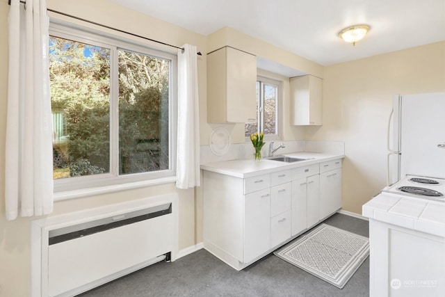 kitchen with white fridge, sink, radiator heating unit, white cabinets, and tile countertops