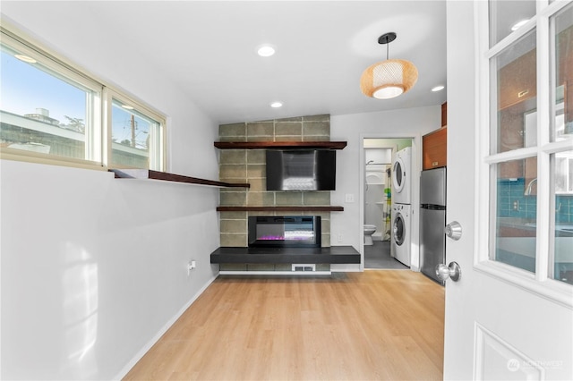 unfurnished living room with stacked washer / dryer, a large fireplace, and light hardwood / wood-style flooring