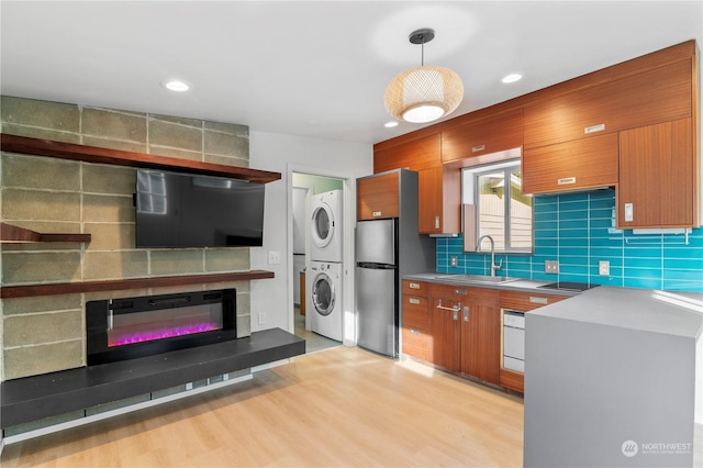 kitchen with sink, stainless steel refrigerator, stacked washer and clothes dryer, tasteful backsplash, and decorative light fixtures