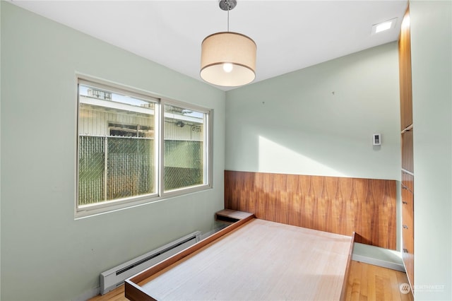 empty room featuring a baseboard heating unit, hardwood / wood-style floors, and wood walls