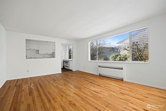 unfurnished living room with radiator, light hardwood / wood-style flooring, and a textured ceiling