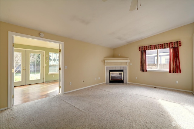 unfurnished living room with french doors, vaulted ceiling, a tile fireplace, and light carpet