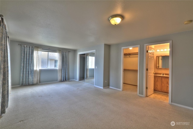 interior space featuring a walk in closet, light carpet, a textured ceiling, and ensuite bath