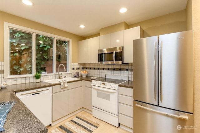 kitchen featuring sink, dark stone countertops, white cabinets, stainless steel appliances, and backsplash