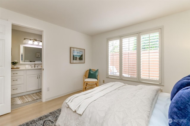 bedroom with ensuite bathroom, sink, and light hardwood / wood-style flooring