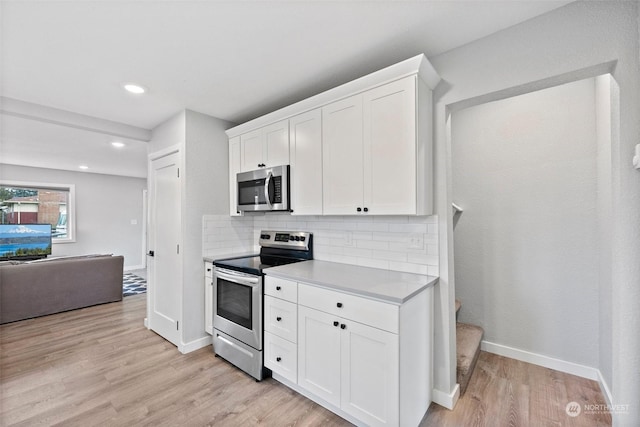 kitchen with appliances with stainless steel finishes, light wood-type flooring, white cabinets, and backsplash