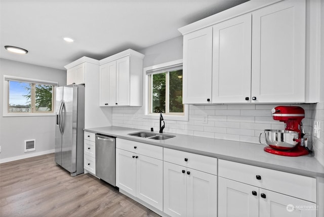 kitchen with sink, white cabinetry, light wood-type flooring, appliances with stainless steel finishes, and decorative backsplash