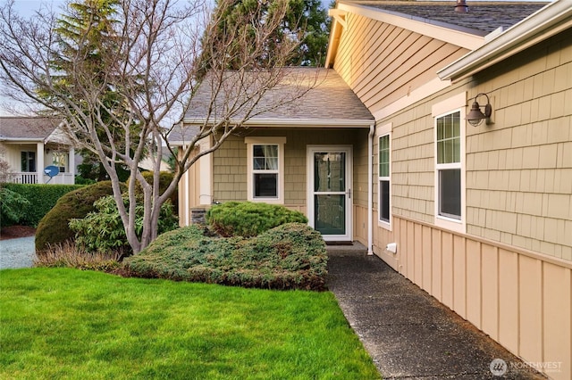 entrance to property with a shingled roof and a lawn