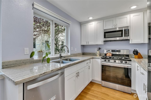 kitchen with white cabinets, light wood-style flooring, appliances with stainless steel finishes, light stone countertops, and a sink