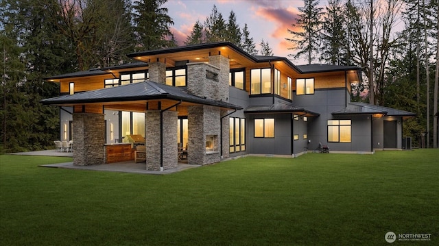 back house at dusk with a yard, exterior bar, an outdoor kitchen, and a patio area