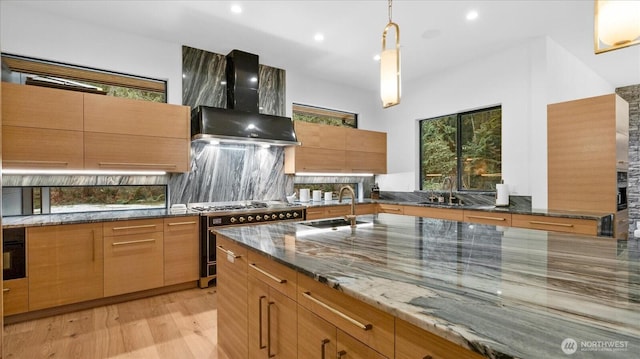 kitchen featuring wall chimney exhaust hood, stone counters, high end stove, backsplash, and sink