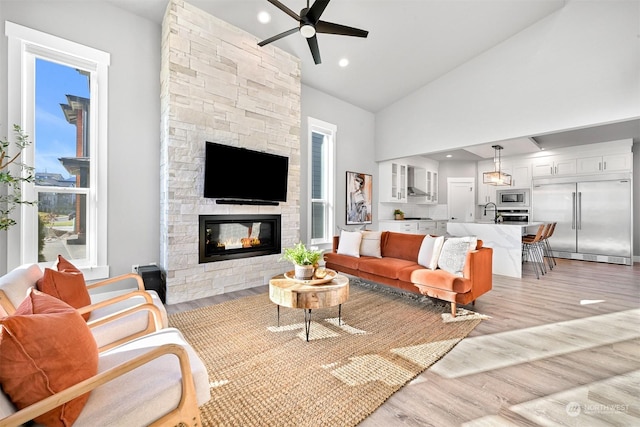 living room featuring ceiling fan, a fireplace, high vaulted ceiling, and light hardwood / wood-style flooring