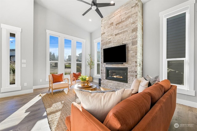 living room with hardwood / wood-style flooring, ceiling fan, a stone fireplace, and vaulted ceiling