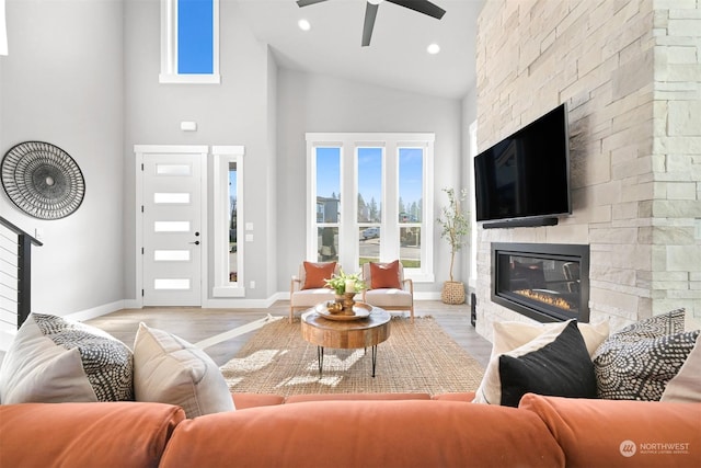 living room with a stone fireplace, high vaulted ceiling, ceiling fan, and light wood-type flooring